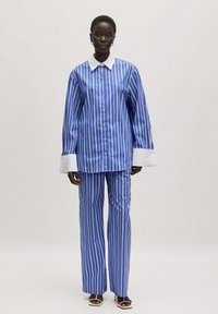 Blauw-wit gestreepte oversized blouse met een witte kraag en manchetten, gedragen met bijpassende gestreepte wijde broek. Glad stoftextuur.