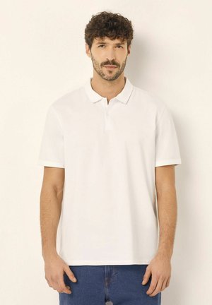 Witte polo met een kraag, gemaakt van katoen, met korte mouwen en een knopensluiting. Gekleed met blauwe denim jeans.