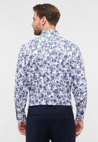 Langsleeve shirt met een blauw bloemenpatroon op een witte achtergrond, met een kraag en knoopmanchetten.