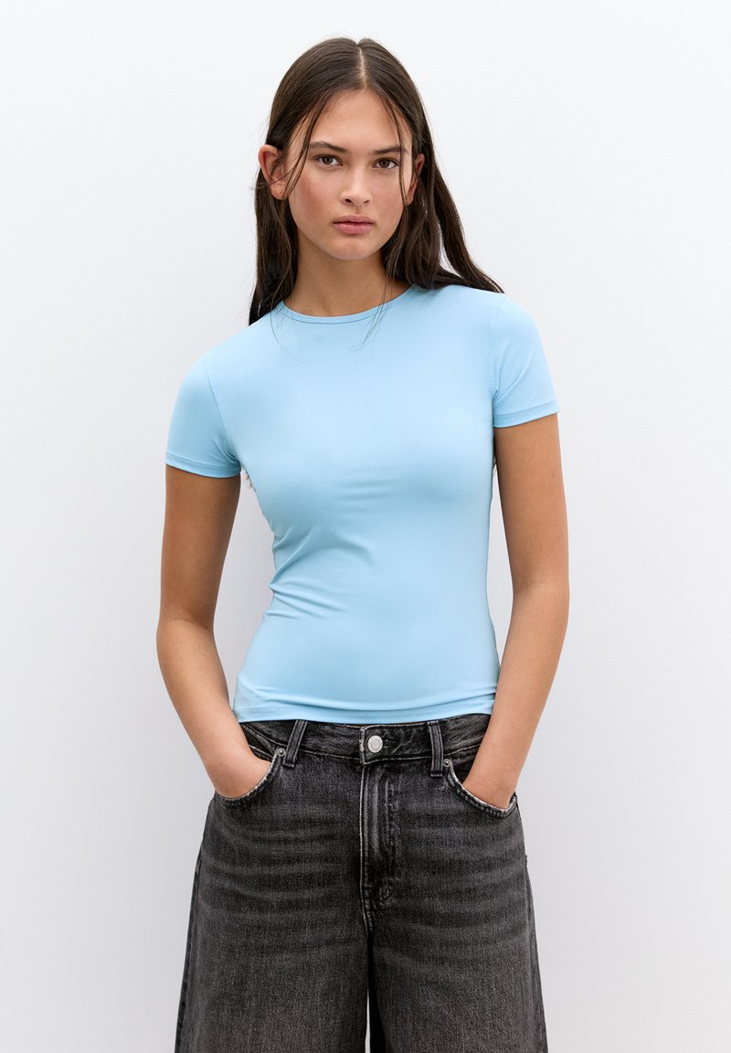 Világoskék, rövid ujjú, sima anyagú felső, kerek nyakkivágással, magas derekú, fekete farmernadrággal párosítva, oldalsó zsebekkel.