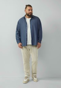 Casual outfit met een blauwe overhemden over een wit T-shirt, gecombineerd met crèmekleurige corduroy broeken en lichte sneakers.