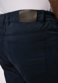 Námořnické modré kalhoty s texturovanou tmavou koženou nášivkou s nápisem "BOSTON PARK". Mají elastický pás a detaily na zadních kapsách.