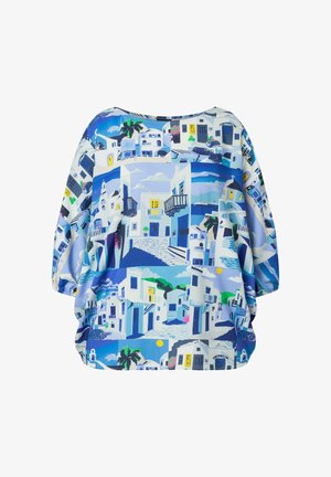 Loose long-sleeve blouse with blue and white Mediterranean village print featuring white buildings, balconies, palm trees, and cobblestone streets.