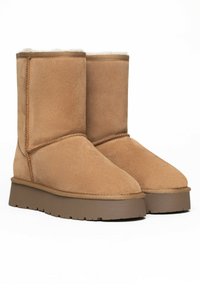 Botines de ante en tono beige con un forro interior suave, puntera redondeada y una suela de goma texturizada. Presentan costuras visibles y un tacón bajo.