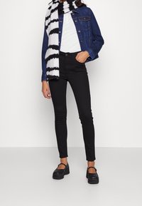 Jeans skinny neri, una giacca di jeans blu e una sciarpa a righe bianco e nero. L'outfit è abbinato a delle scarpe con piattaforma nere.