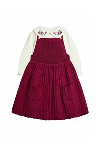 Camisa blanca de manga larga con cuello bordado de flores, combinada con un vestido de tirantes burdeos de punto que cuenta con bolsillos frontales y falda plisada.