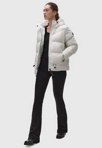 Giacca a vento bianca con cappuccio, design trapuntato, zip frontale e dettagli con cordino. Top e pantaloni aderenti neri, abbinati a stivaletti neri chunky.