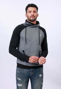 Szara i czarna bluza z kapturem oraz kieszenią kangurzą, z złotym logo na piersi i teksturowanym materiałem. Nosi się z przetartymi dżinsami.