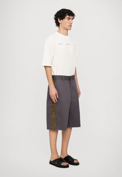 Gray shorts with leopard print side panel, paired with a cream short-sleeve shirt. Worn with black sandals. Smooth texture, relaxed fit.