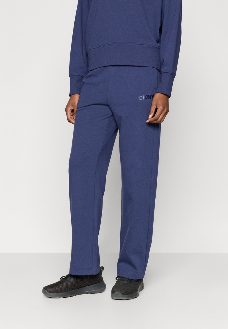 Tmavomodré tepláky z jemnej tkaniny, s voľným strihom, bočnými vreckami a jemným logom DKNY na prednej strane.