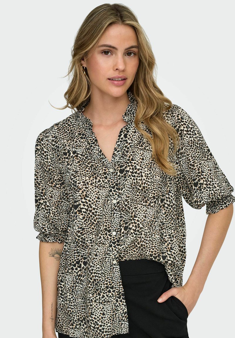 Camisa de botones de manga corta en tejido transparente con un estampado de leopardo en negro y beige. Presenta un cuello con volantes y un corte relajado.