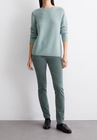 Světle zelený pletený svetr s širokým výstřihem a dlouhými rukávy, doplněný o odpovídající zelené slim-fit kalhoty a černé nazouvací boty.