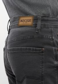 Jeans grigio scuro in denim, dotati di un'etichetta in pelle con "INDICODE" e "EST. 1993", cuciture visibili e un design slim fit.