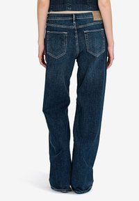 Široké džínové kalhoty tmavé wash vyrobené z denimu. Mezi jejich vlastnosti patří dvě zadní kapsy s charakteristickým tvarem a kožená nášivka s logem na pase.