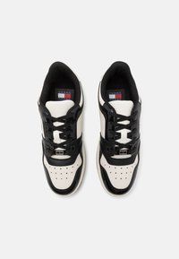 Paire de baskets basses noires et blanches avec embout perforé et lacets noirs, vue de dessus sur fond blanc.
