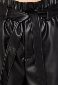 Černé kožené kalhoty s vysokým pasem, širokým zavazovacím pásem a plisovanou texturou. Hladký povrch s elastickými detaily v oblasti pasu.