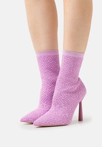 Růžové pletené kotníkové boty s geometrickým vzorem, špičaté špičky a 10 cm stiletto podpatky. Měkká textura a přiléhavý design.