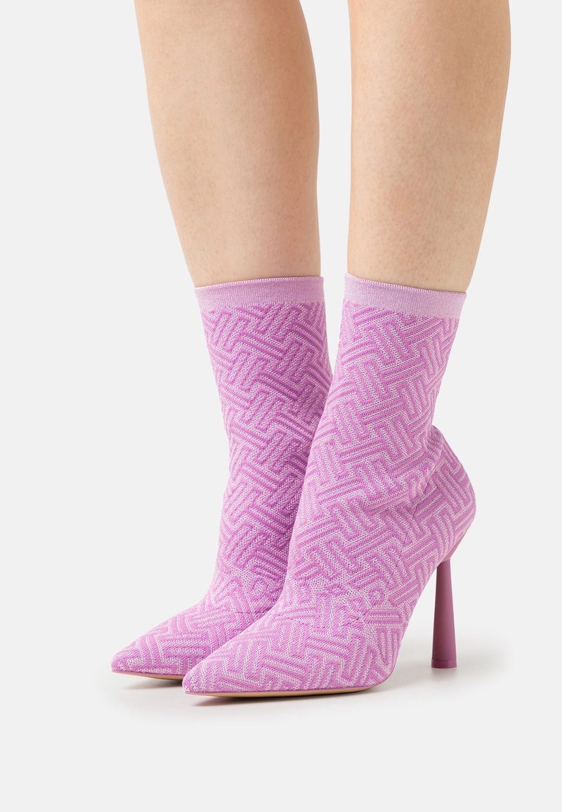 Růžové pletené kotníkové boty s geometrickým vzorem, špičaté špičky a 10 cm stiletto podpatky. Měkká textura a přiléhavý design.