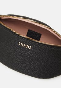 Schwarze Ledertasche mit strukturierter Oberfläche, goldener Reißverschluss und LIU JO-Logo in Gold auf der Außenseite. Das Innere ist mit einem hellrosa Futter ausgestattet.