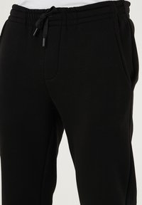 Schwarze Sweatpants aus weichem Stoff, mit elastischem Bund und Kordelzug, Seitentaschen und schmal zulaufenden Beinen.