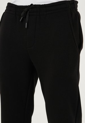 Pantaloni tuta neri realizzati in un tessuto morbido, con vita elasticizzata e coulisse, tasche laterali e gamba tapered.