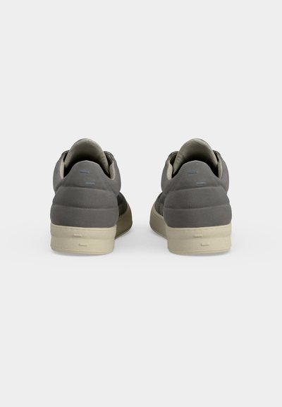 Paire de baskets basses grises avec cols rembourrés et semelles blanches vues de dos sur un fond clair uni.