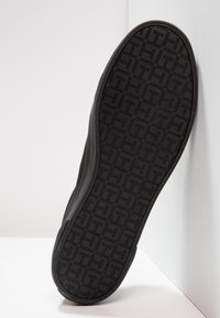 Suola di sneaker nera con una superficie texture e un motivo geometrico. Il bordo è leggermente sollevato, mettendo in risalto il materiale in gomma e il design.