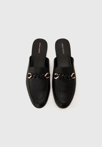Black leather slip-on shoes with a flat sole, featuring a prominent chain accent in black and gold across the vamp. Smooth texture.