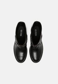 Bottines noires en matériau brillant avec texture crocodile. Elles comportent une sangle décorative sur le dessus et un design à bout rond.