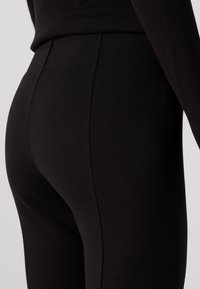 Svarta leggings tillverkade av stretchtyg. De har en slät yta, �åtsittande form och har sömdetaljer längs sidorna.
