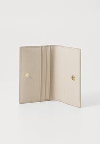 Beige leather wallet with textured exterior. Features slots for cards and a gold snap closure. Interior is smooth with minimalist design.