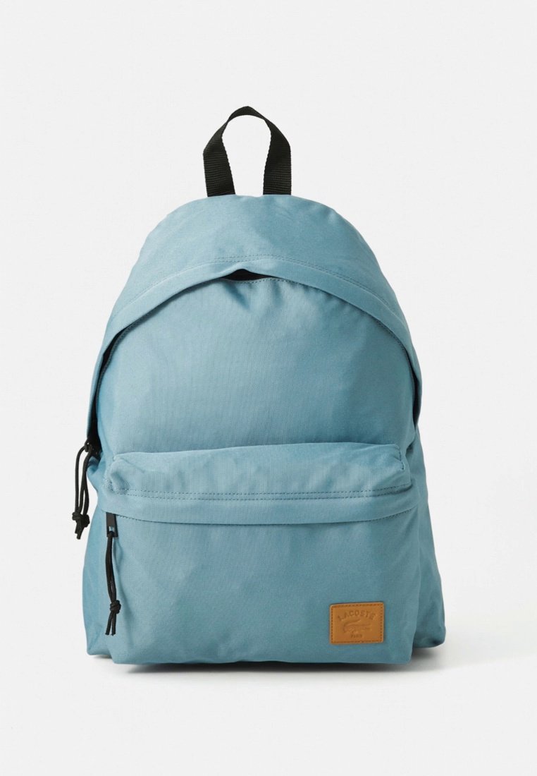 Sac à dos bleu clair en tissu, doté d'une fermeture à cordon, d'une poche zippée frontale et d'un patch logo en cuir marron.