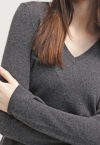 Szary sweter w serek, wykonany z miękkiego materiału, z długimi rękawami wykończonymi ściągaczami i gładką fakturą, owinięty wokół ramion.