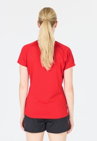 Röd atletisk T-shirt med en slät textur och korta ärmar, med en rundad halsringning och en lätt svans vid fållen.