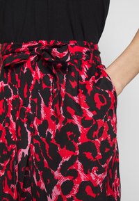 Rote und schwarze Leopardenprint-Hosen mit einer Schleife am Bund, Seitentaschen und einem leichten Stoff. Sie bieten eine lockere Passform und ein fließendes Design.