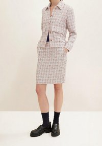Costume en tweed avec une veste courte et une jupe mi-longue en blanc avec des accents rouges et bleus. Caractéristiques : fermeture à boutons et poches latérales. Chaussures noires portées.