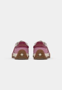 Converse sneakers with pink and maroon upper, white accents, and brown rubber sole featuring a star detail on the heel.
