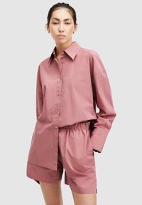 Conjunto de camisa abotonada y pantalones cortos de algodón en rosa claro. La camisa tiene cuello y mangas largas; los pantalones cortos cuentan con una cintura elástica.