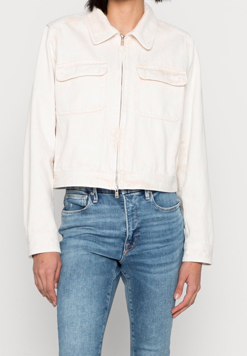 Avkortad vit denimjacka med krage, framdragkedja och två bröstfickor. Mjuk textur med en subtil blekt utseende.