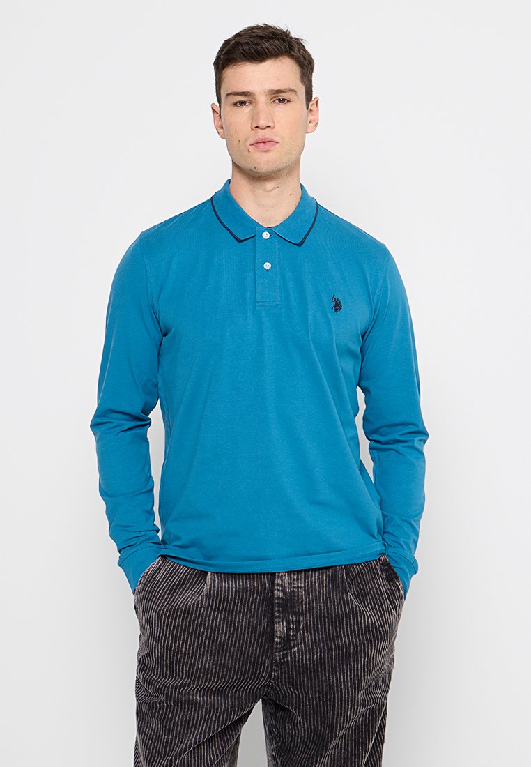 Polo a maniche lunghe di un brillante teal, con colletto, due bottoni all'altezza del collo e un piccolo logo sul lato sinistro del petto. Tessuto strutturato.