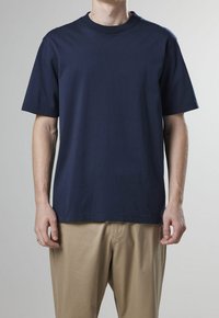 Námorně modré bavlněné tričko s klasickým kulatým výstřihem, krátkým rukávem a volným střihem. Hladká textura, bez vzorů nebo ozdob.