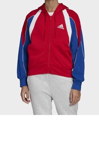 Sudadera con cremallera roja y azul con detalles en blanco, hecha de tela suave, que cuenta con capucha y el logo de Adidas en el pecho.