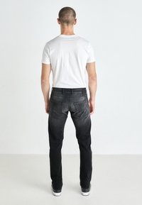 Black denim jeans with a faded finish, straight leg design, two back pockets, and a classic belt loop waistband. Model wears a white t-shirt.