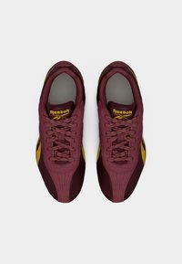 Ζευγάρι ματζέντα και κίτρινα αθλητικά παπούτσια Reebok με κορδόνια, από πάνω σε απλό λευκό φόντο.