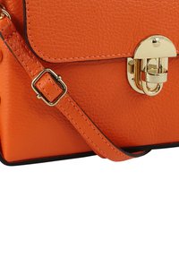 Oranje leren handtas met een gestructureerde afwerking, voorzien van een gouden sluiting, verstelbare riem en zwarte randafwerking. Compact rechthoekig ontwerp.