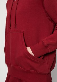 Maroon pullover hoodie made of soft cotton blend, featuring a front pocket, adjustable drawstrings, and ribbed cuffs with textured finish.