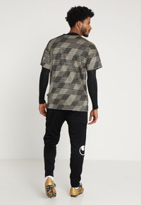 Zwart en beige sportoutfit met een gestreepte top met korte mouwen en aansluitende lange mouwen, gecombineerd met zwarte broek met een logo en accenten.