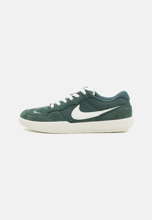 Vihreä mokkanahkainen matalakärkinen lenkkari, jossa valkoinen Nike-swoosh-merkki, valkoiset nauhat ja luonnonvalkoinen, pilkullinen pohja, kuvattuna sivulta valkoisella taustalla.