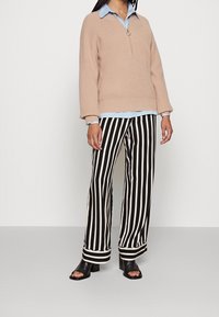 Beige knitted pullover with zip neck over a light blue collared shirt, paired with black and white striped wide-leg pants and black open-toe heels.