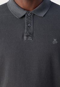 Polo gris foncé avec deux boutons et lettres brodées "MOP" sur la poitrine gauche porté par une personne.